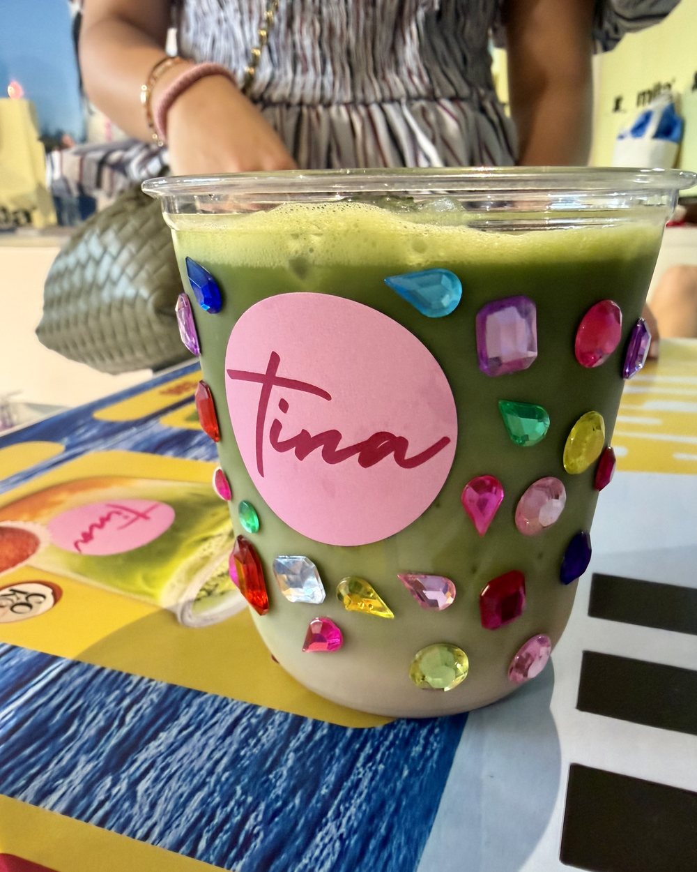 Vaso de matcha de VeryMatcha cubierto de piedras de colores, con el sticker rosado de Tina