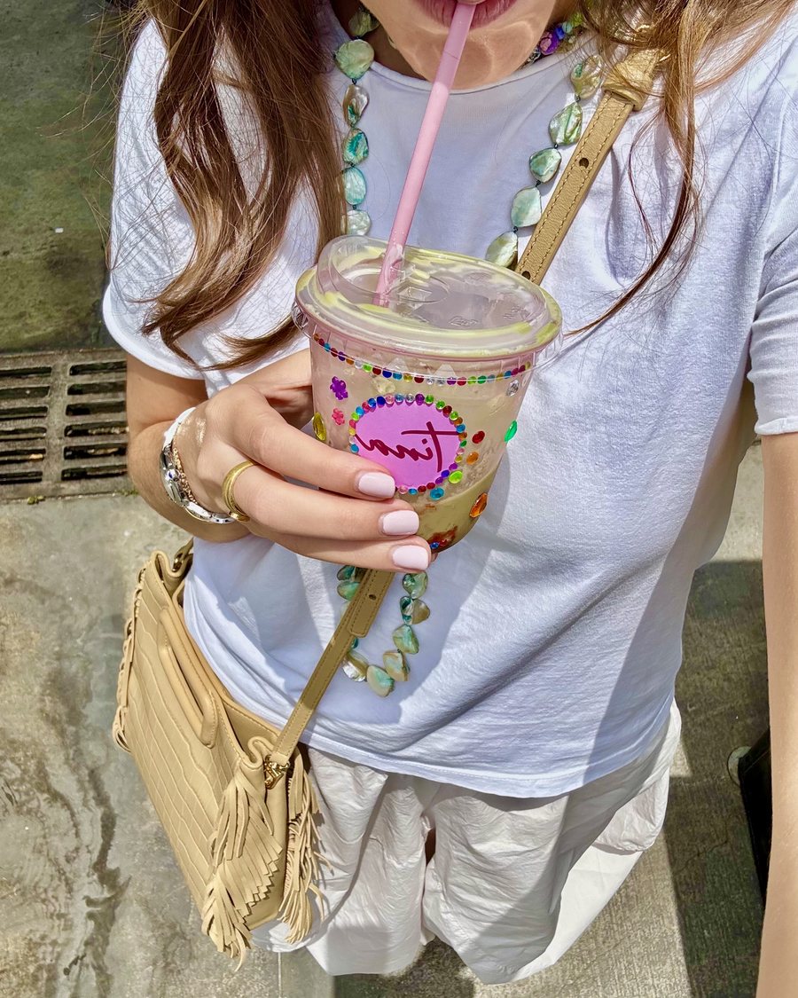 Mujer sosteniendo un vaso de matcha con pedrería, en el pop-up