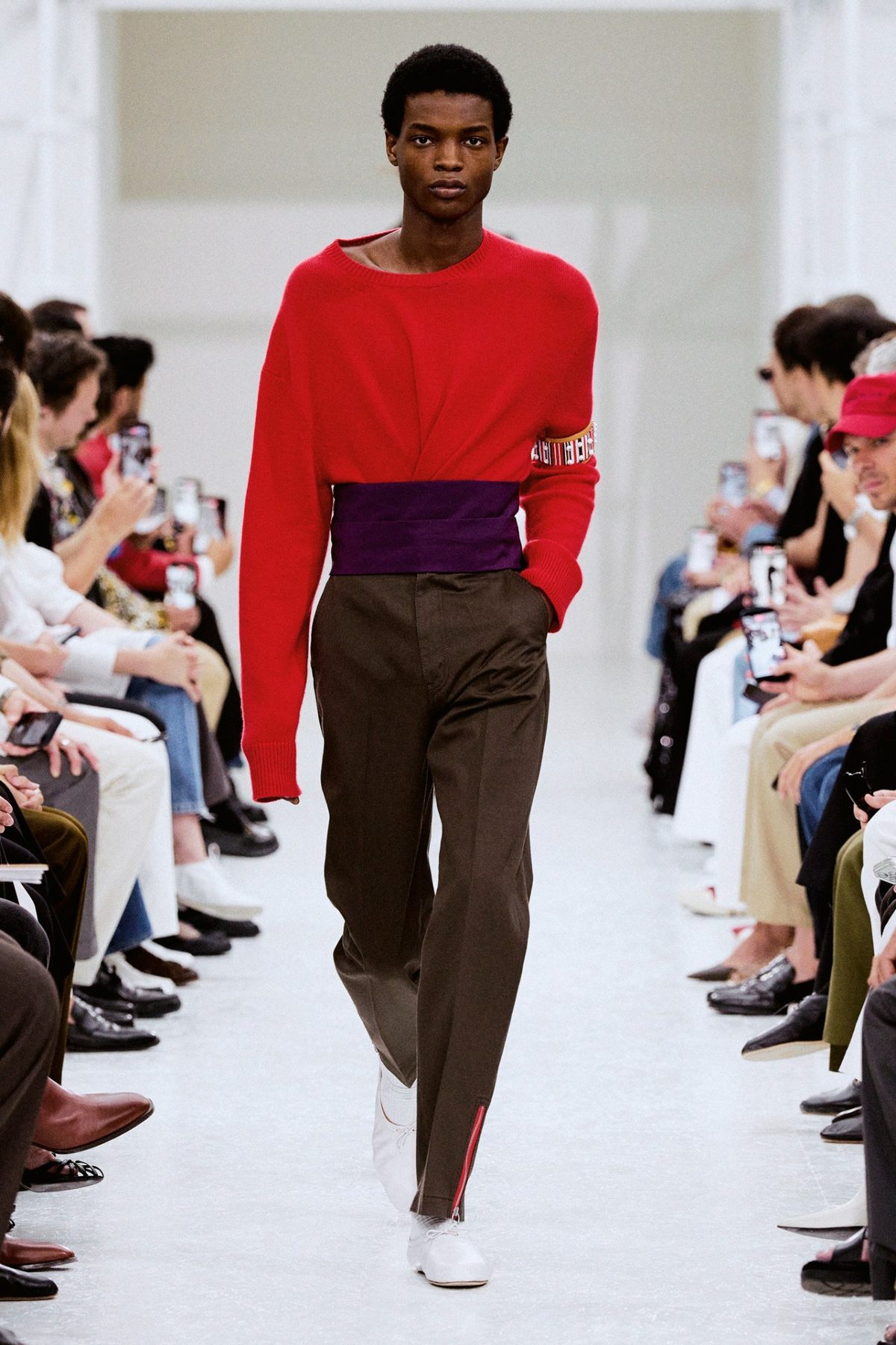 Modelo de Celine con suéter rojo, fajín morado y pantalón marrón en la pasarela de primavera 2027