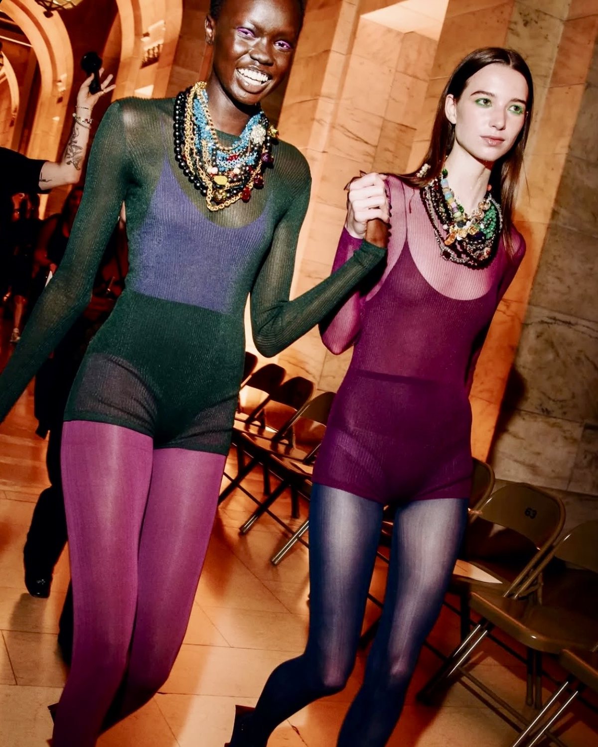 Dos modelos riendo con bodies de punto transparente y collares de piedras de colores