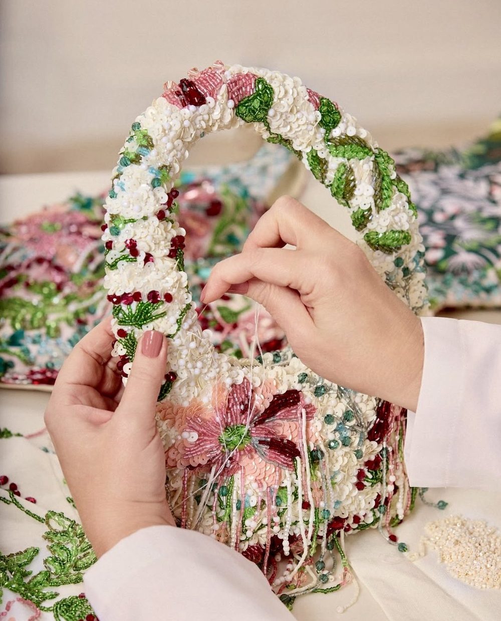 Manos bordando una cartera de cuentas con flores rosadas y hojas verdes