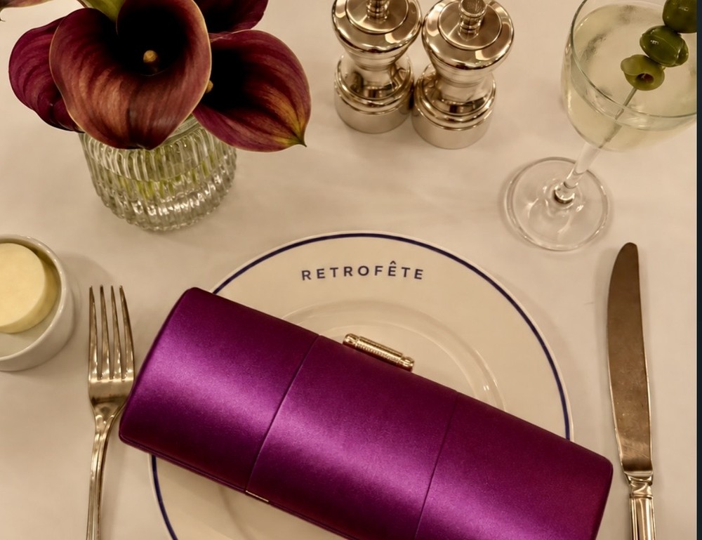 Mesa puesta con un plato que dice Retrofête y una cartera de raso morada